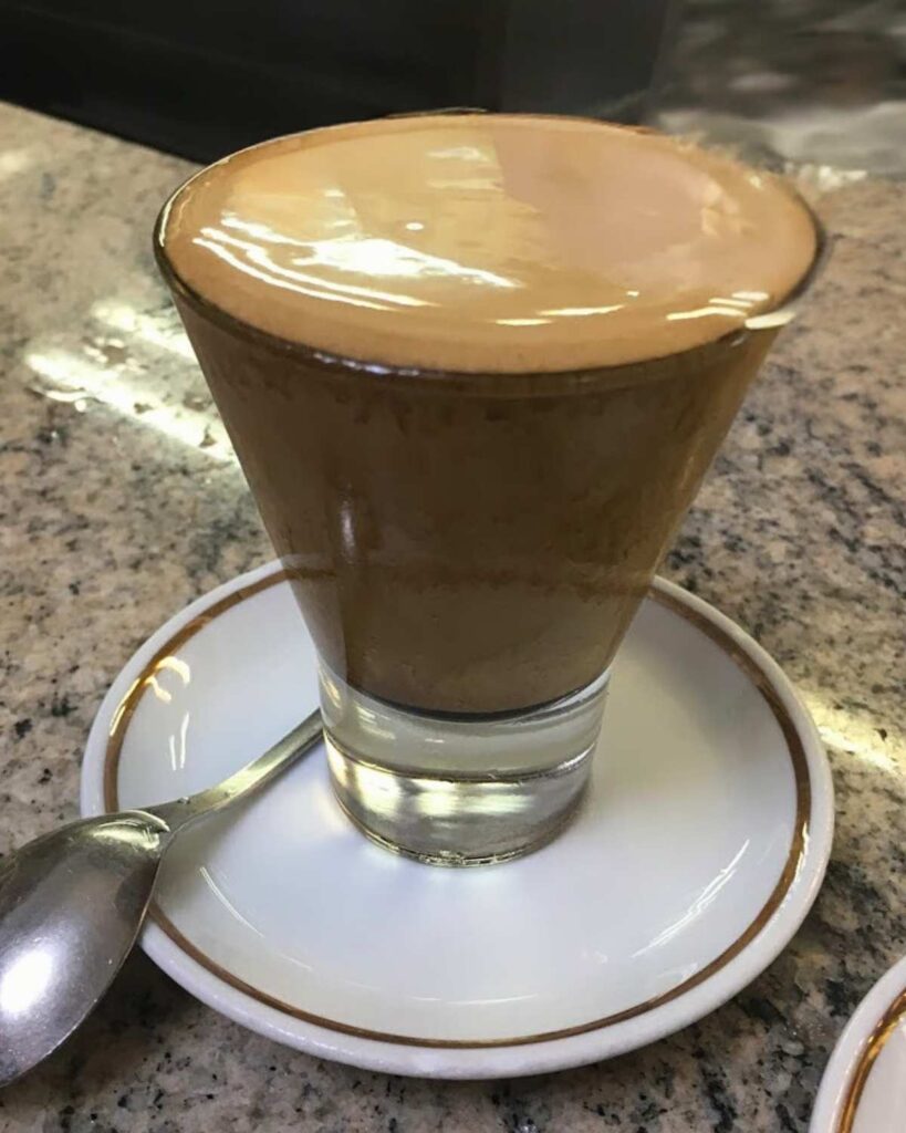 A creamy, frothy coffee served in a clear glass at Il Gusto del... Relax, showcasing the neapolitan coffee and coffee in Naples experience.