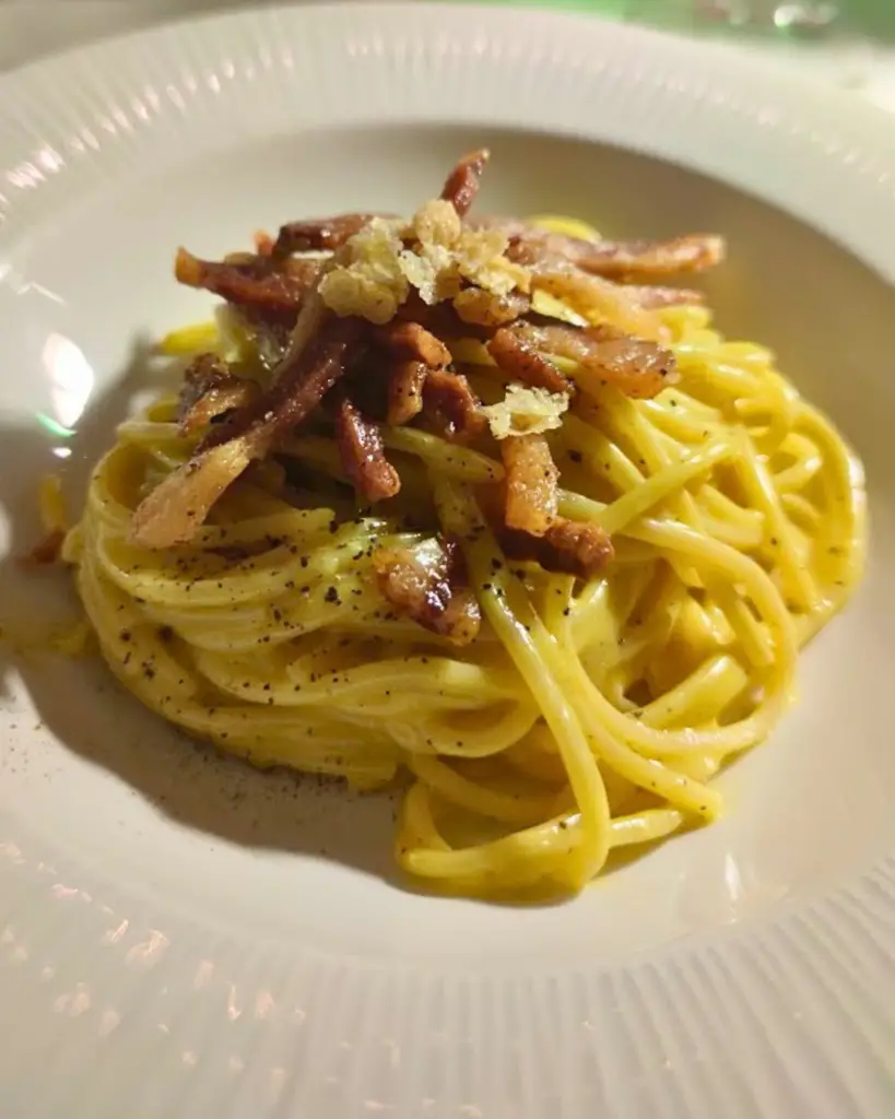 A plate of authentic carbonara pasta at Antica Pesa in Rome, featuring perfectly cooked spaghetti alla chitarra, creamy sauce, and crispy guanciale strips, showcasing the best carbonara pasta in Rome with a true carbonara Rome aesthetic.