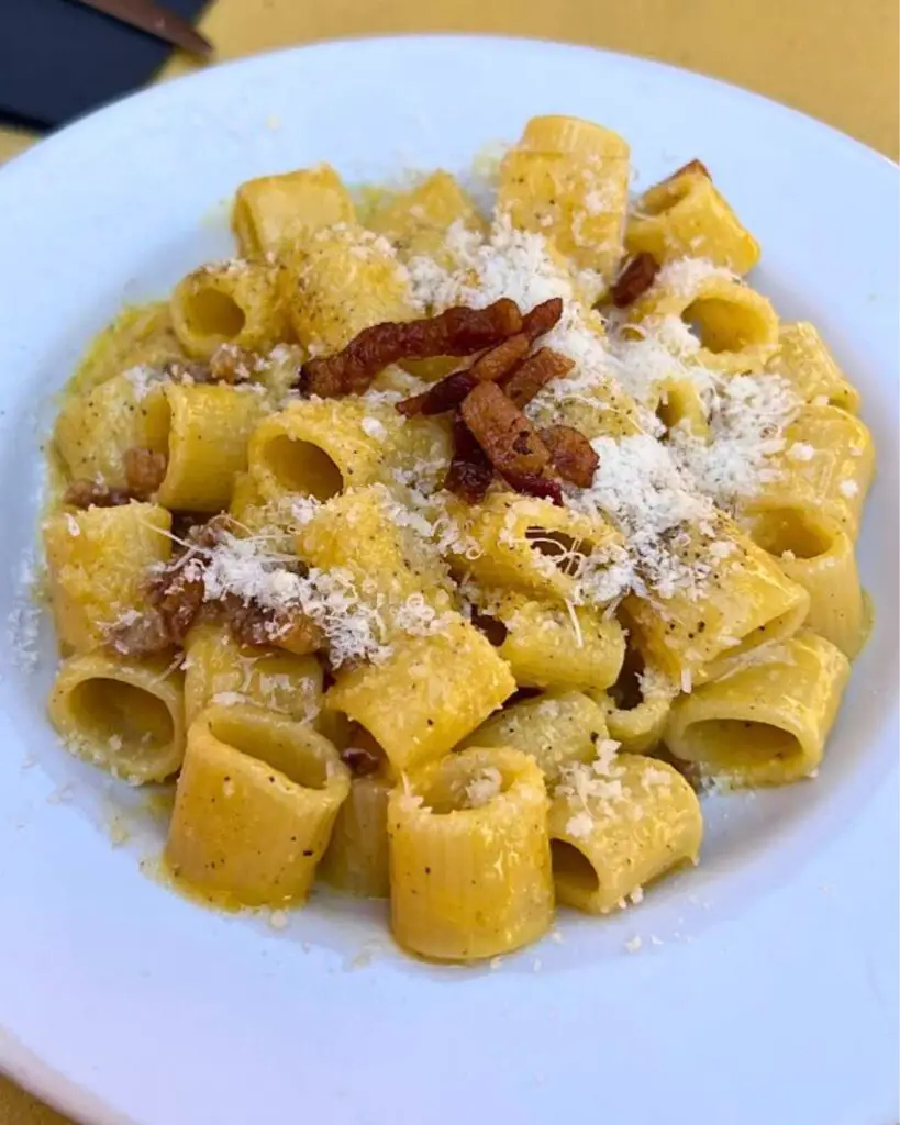 A plate of carbonara pasta in Rome at L'Osteria della Trippa, featuring rigatoni with creamy sauce and crispy bacon, highlighting the best authentic carbonara in town.