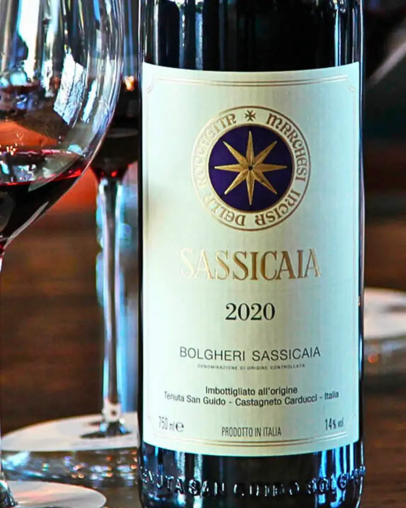 A bottle of Sassicaia 2020, a renowned Supertuscan wine, accompanied by wine glasses, representing the high quality and rich heritage of Italian wines.