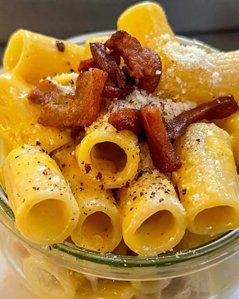 A glass jar filled with carbonara pasta in Rome at Eggs, featuring rigatoni with creamy sauce and crispy bacon, highlighting one of the best pasta place in rome.