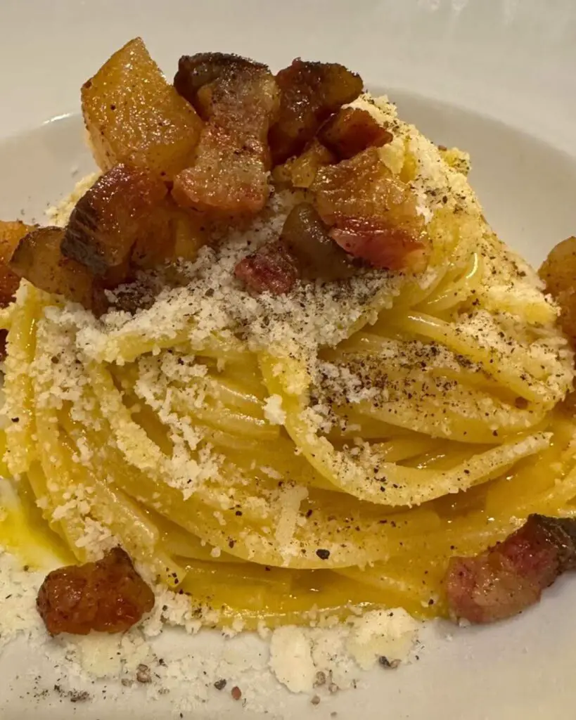 A plate of spaghetti carbonara Rome at Hosteria Grappolo D'Oro, featuring creamy pasta with large, crispy guanciale pieces, and a generous sprinkle of Pecorino Romano, showcasing the carbonara Rome aesthetic.