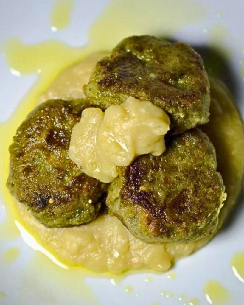 Close-up of three chickpea patties on a bed of creamy sauce with a drizzle of olive oil, served at Le Bistrot, a popular vegan restaurant in Rome.