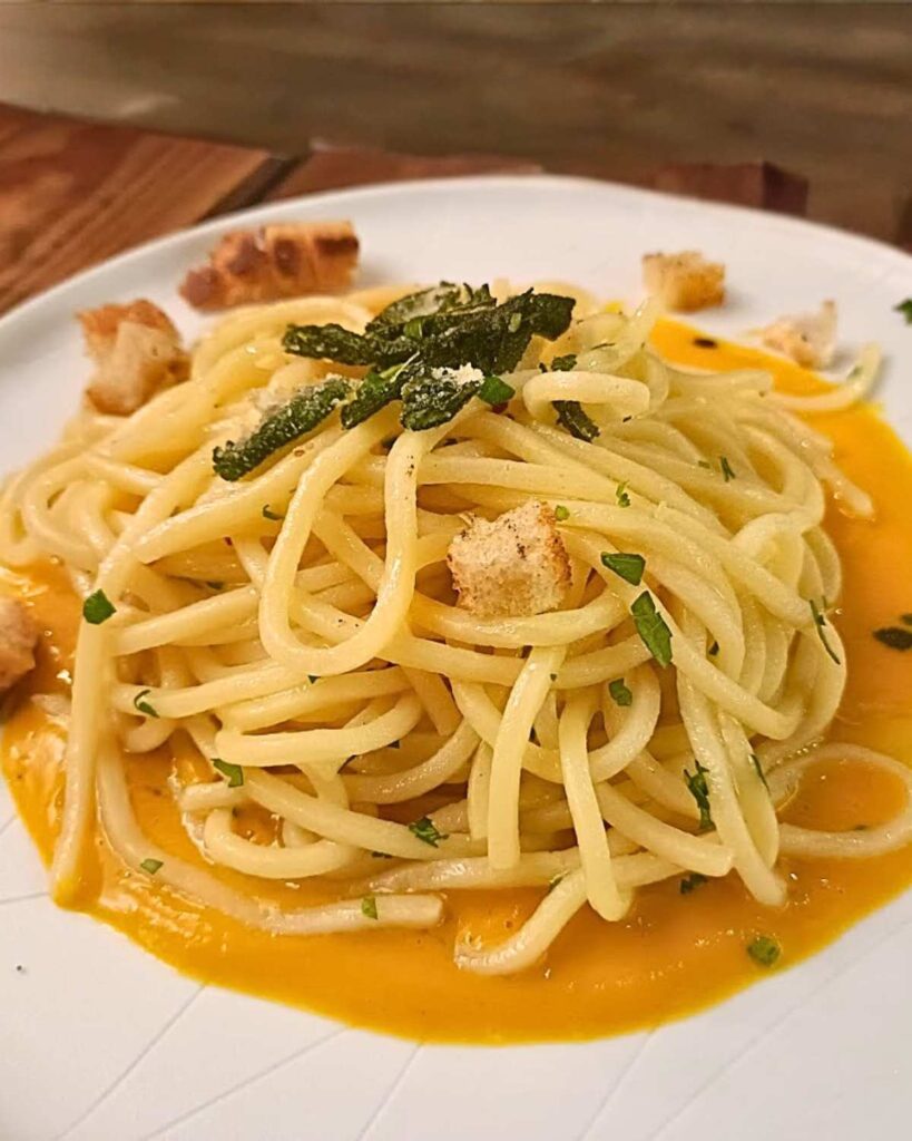 Plate of vegan spaghetti with creamy sauce and croutons, garnished with herbs, at Rifugio Romano, a top spot for vegan food in Rome, known for its vegan versions of traditional Roman dishes.