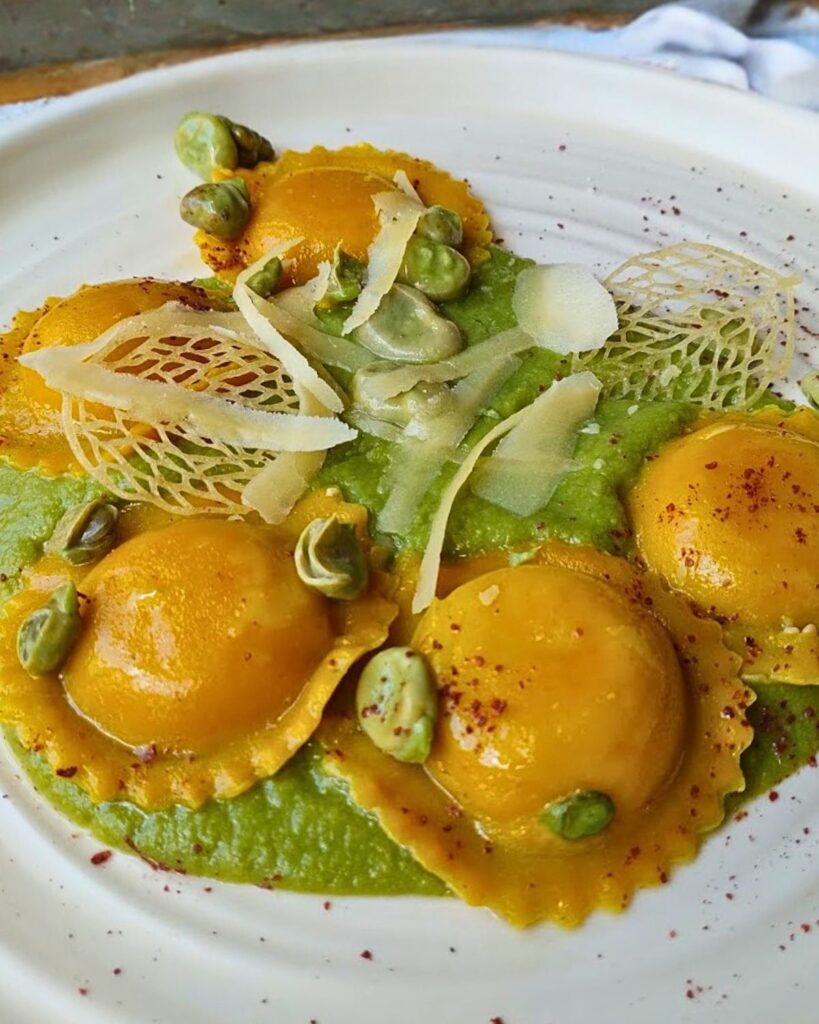 Close-up of yellow tortelli on green truffle potato cream, garnished with broad beans, almond brittle, and shaved cheese at Romeow Cat Bistrot, one of the best vegan restaurants in Rome.