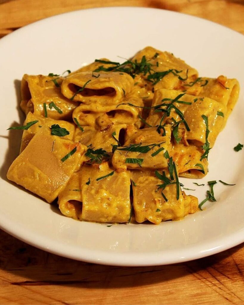 Close-up of vegan pumpkin carbonara pasta garnished with fresh herbs at Status Quo, a top vegan restaurant in Rome.