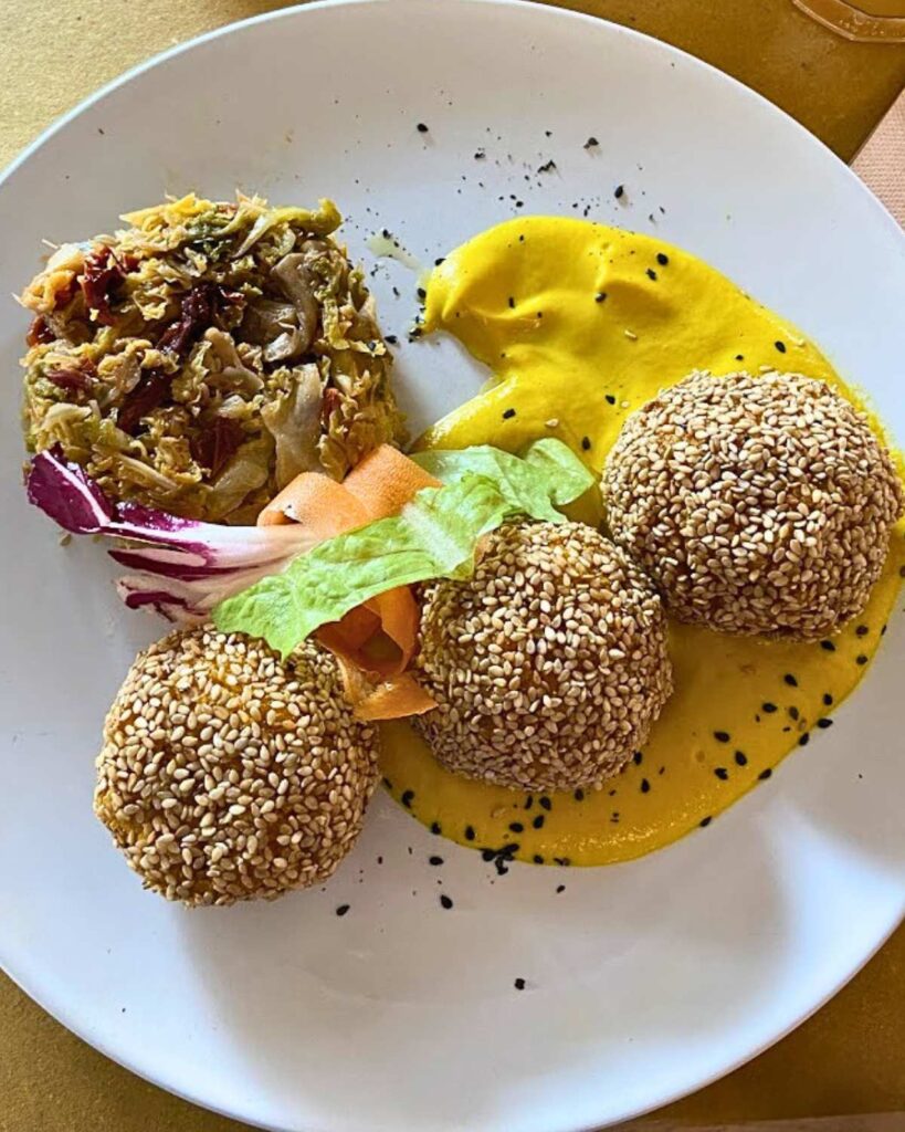 Vegan sesame balls served with a creamy yellow sauce and a side of vegetables at Vitaminas24, a popular vegan restaurant in Rome.