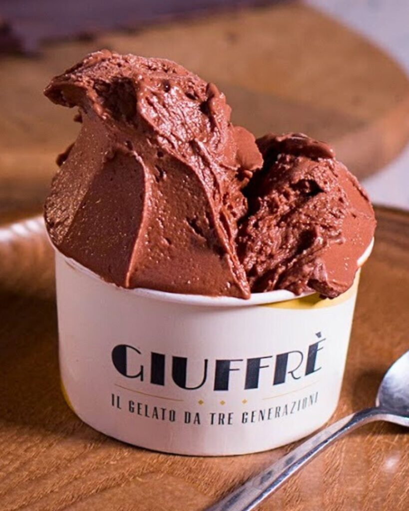 A cup of rich chocolate gelato from Gelateria Giuffrè in Rome, sitting on a wooden plate with a spoon, showcasing the best ice cream in Rome with an inviting gelato aesthetic.