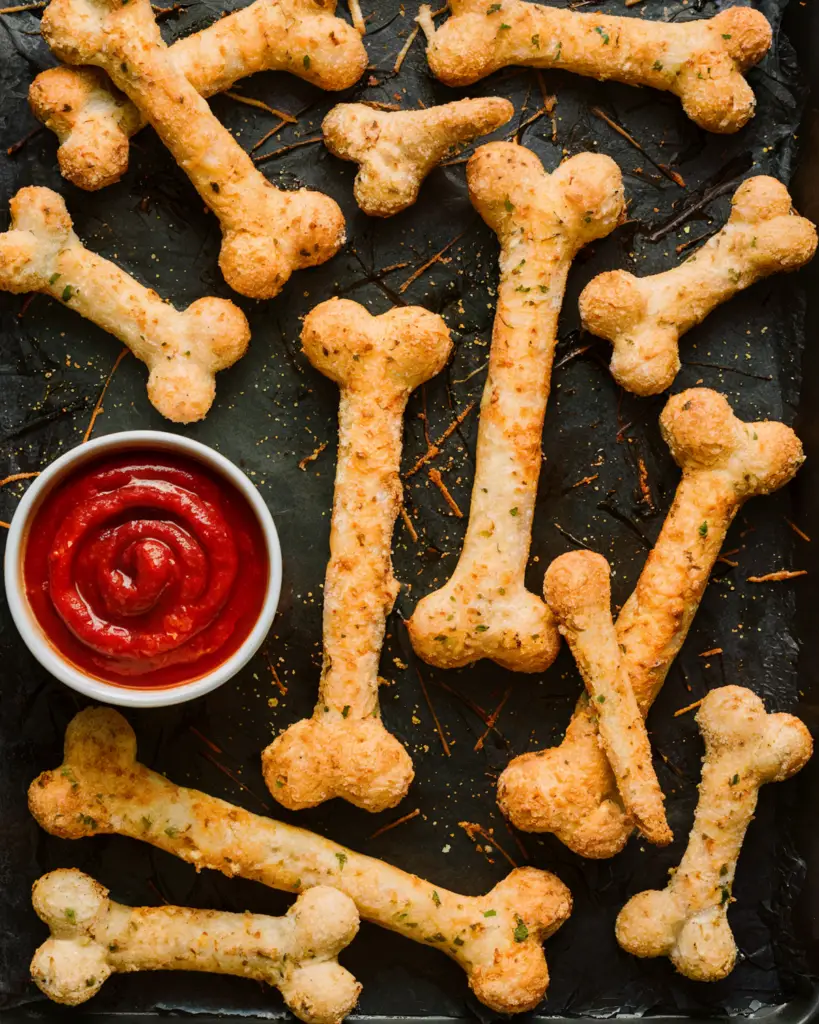 Cheesy breadstick bones with marinara sauce for dipping, perfect for Halloween party appetizers and creepy Halloween food.