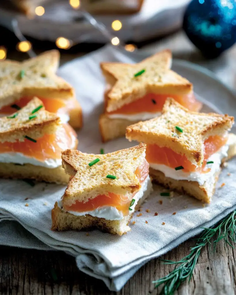 Toasted triangular Pandoro bread sandwiches filled with smoked salmon and creamy robiola cheese, garnished with chives, perfect for Italian finger food appetizers at parties.