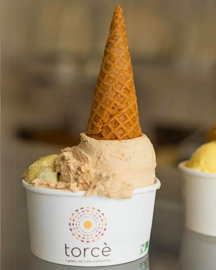 Two cups of gelato from Gelateria Torcè in Rome, each topped with a waffle cone and featuring different flavors, showcasing the best gelato in Rome with an inviting and authentic gelato Rome aesthetic.