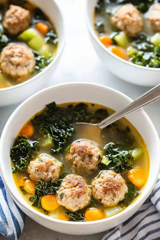 Three bowls of keto Italian wedding soup with large sausage meatballs, vibrant kale, carrots, and a light broth, perfect for healthy eating and fall soup recipes.