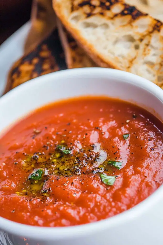 A bowl of roasted tomato basil soup, rich in flavor with herbs and served with a spoon, perfect for a comforting meal.