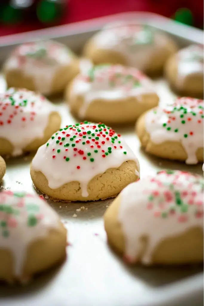 A plate of soft, golden-brown traditional Italian ricotta Christmas cookies, generously topped with a smooth white icing and decorated with festive red and green sprinkles. These Italian Christmas cookies are made with fresh ricotta cheese, creating a moist and fluffy texture, perfect for any holiday celebration, especially for those seeking traditional Italian Christmas cookies recipes.