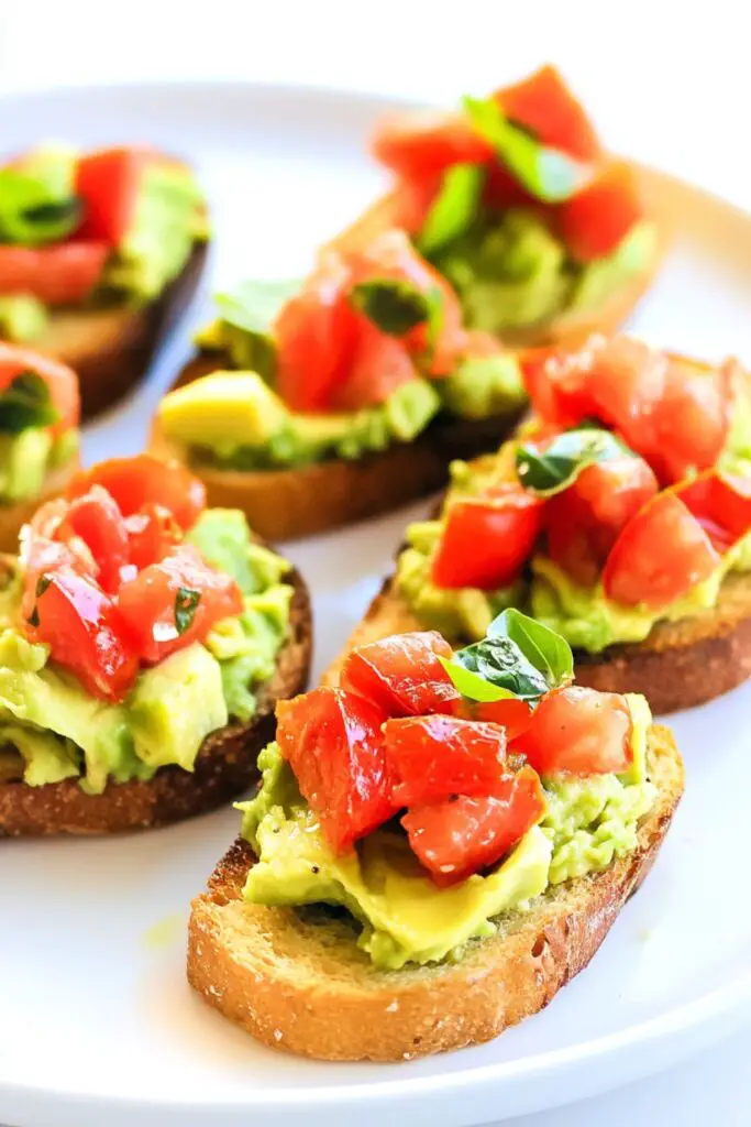 Crispy toasted bread topped with creamy smashed avocado, fresh tomato, and basil, creating a colorful avocado bruschetta appetizer with a healthy twist.