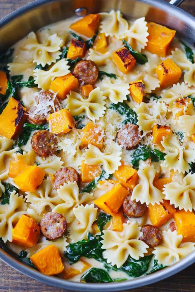 A skillet of creamy roasted butternut squash pasta with Italian sausage and spinach, topped with melted parmesan cheese.