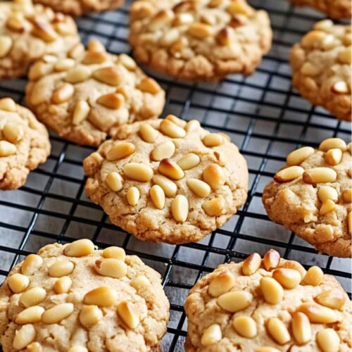 Golden-brown Italian Pignoli cookies cooling on a wire rack, covered in toasted pine nuts. These traditional Christmas cookies are a favorite for their almond flavor and crunchy texture.