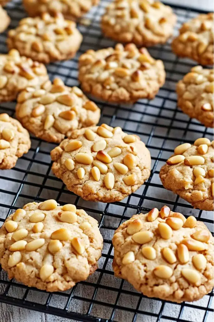 Golden-brown Italian Pignoli cookies cooling on a wire rack, covered in toasted pine nuts. These traditional Christmas cookies are a favorite for their almond flavor and crunchy texture.