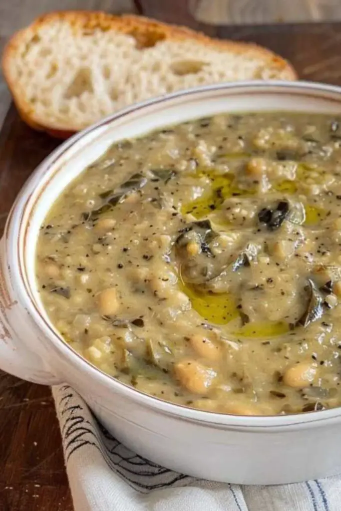 A rustic bowl of thick bean and black cabbage soup drizzled with olive oil, served with slices of Tuscan bread.