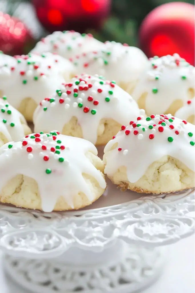 A close-up of homemade traditional Italian anise Christmas cookies, soft and round, covered with a smooth white glaze and topped with colorful nonpareils sprinkles. These authentic Italian Christmas cookies feature a moist, cake-like texture, flavored with anise, and are perfect for anyone looking for traditional Italian Christmas cookies recipes.