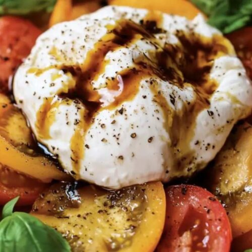 Heirloom Italian Burrata Caprese Salad featuring vibrant slices of red and yellow heirloom tomatoes, fresh basil, and creamy burrata cheese topped with balsamic glaze, perfect for a traditional Italian Christmas side dish.