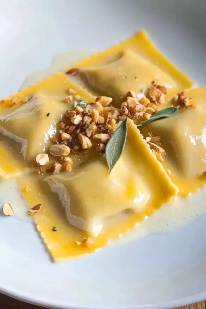 Creamy butternut squash ravioli topped with white wine sauce and sprinkled with chopped hazelnuts, served on a white plate, perfect for an Italian-themed Christmas dinner.