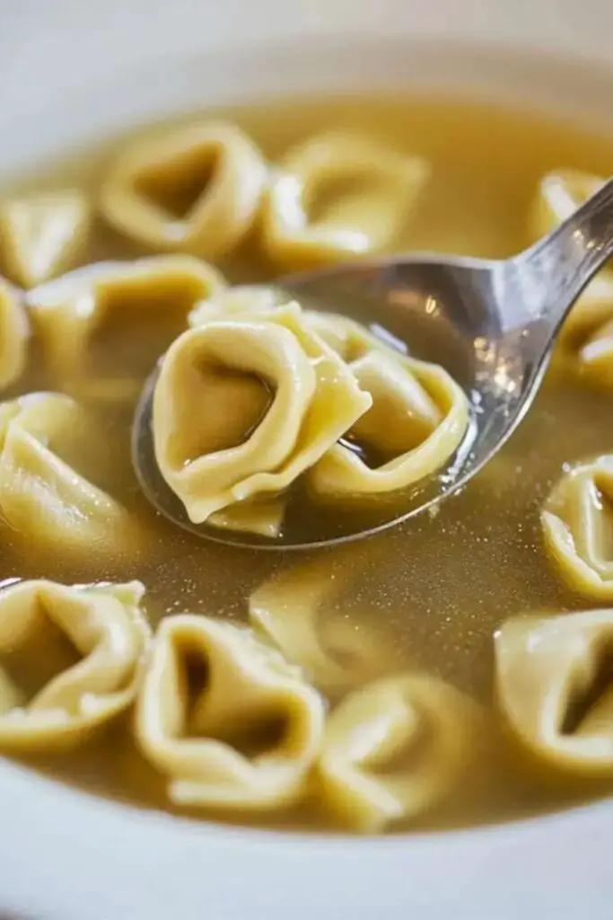 A spoon lifting traditional tortellini from a savory broth, showcasing the classic Italian dish perfect for a Christmas Italian-style meal.