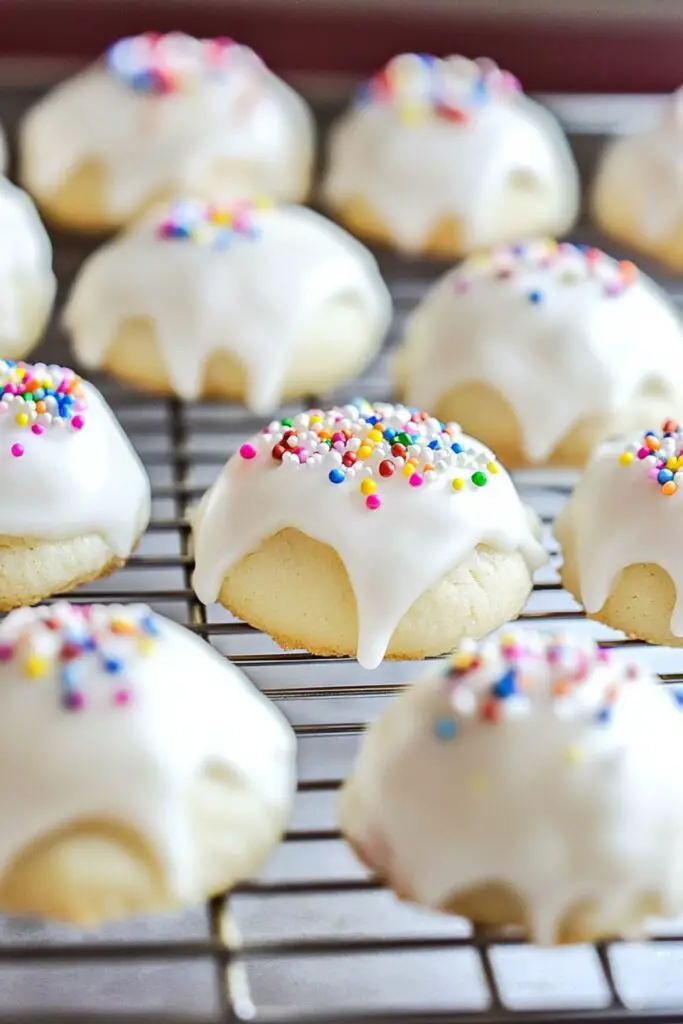 A display of soft Italian wedding cookies with white glaze and colorful sprinkles arranged on a cooling rack.