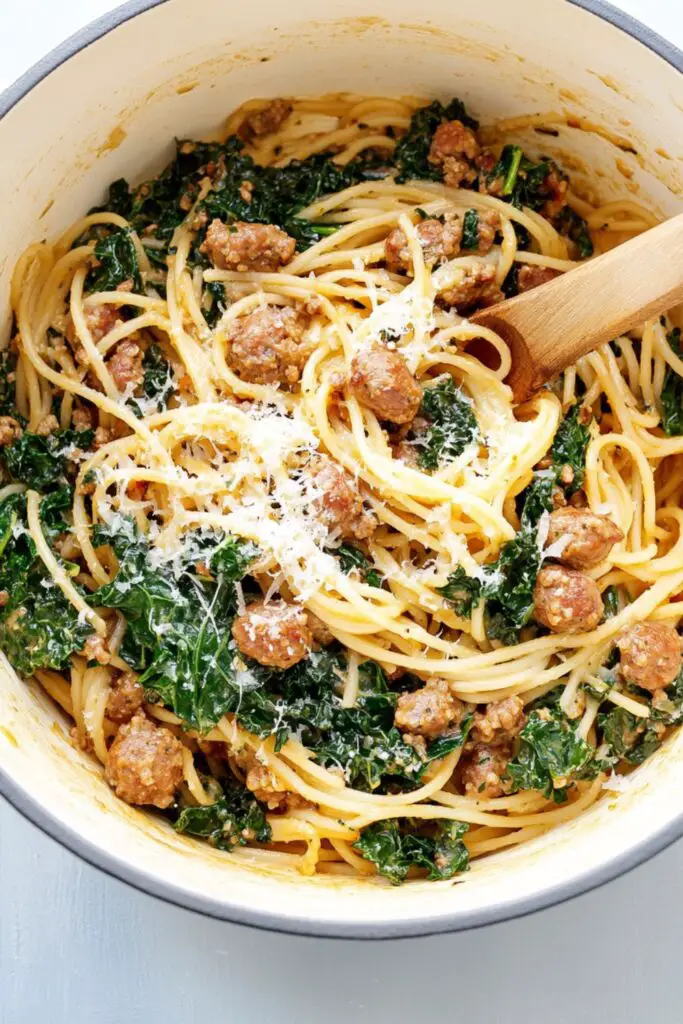 A creamy one-pot pasta dish with Italian sausage, kale, and spaghetti, garnished with grated parmesan cheese in a white Dutch oven.