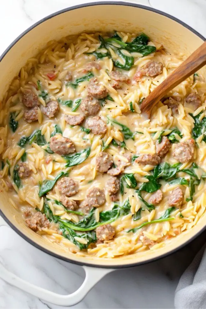 A pot of creamy orzo pasta with Italian sausage and spinach, ready to be served.