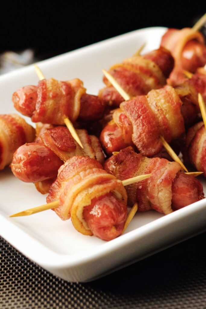 Crispy bacon-wrapped little smokies skewered with toothpicks and arranged on a serving plate. Perfect for a holiday appetizer at a Christmas party.