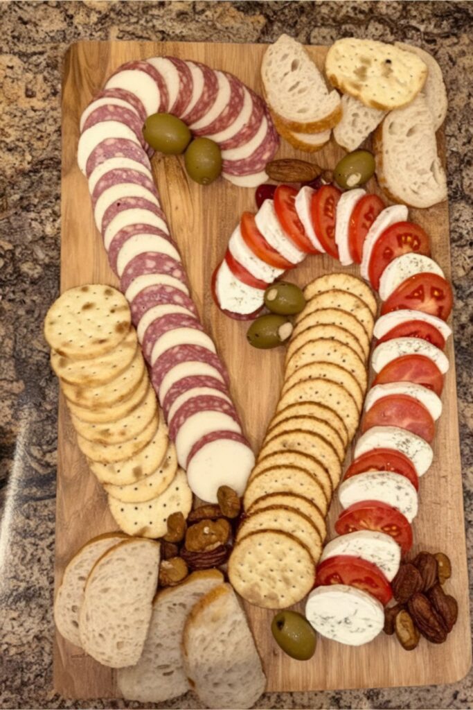 A festive charcuterie board arranged with two candy cane-shaped rows, one with mozzarella and tomato slices, and the other with salami and cheese. The board includes crackers, bread slices, olives, and nuts, making it a perfect addition to a Christmas party buffet.