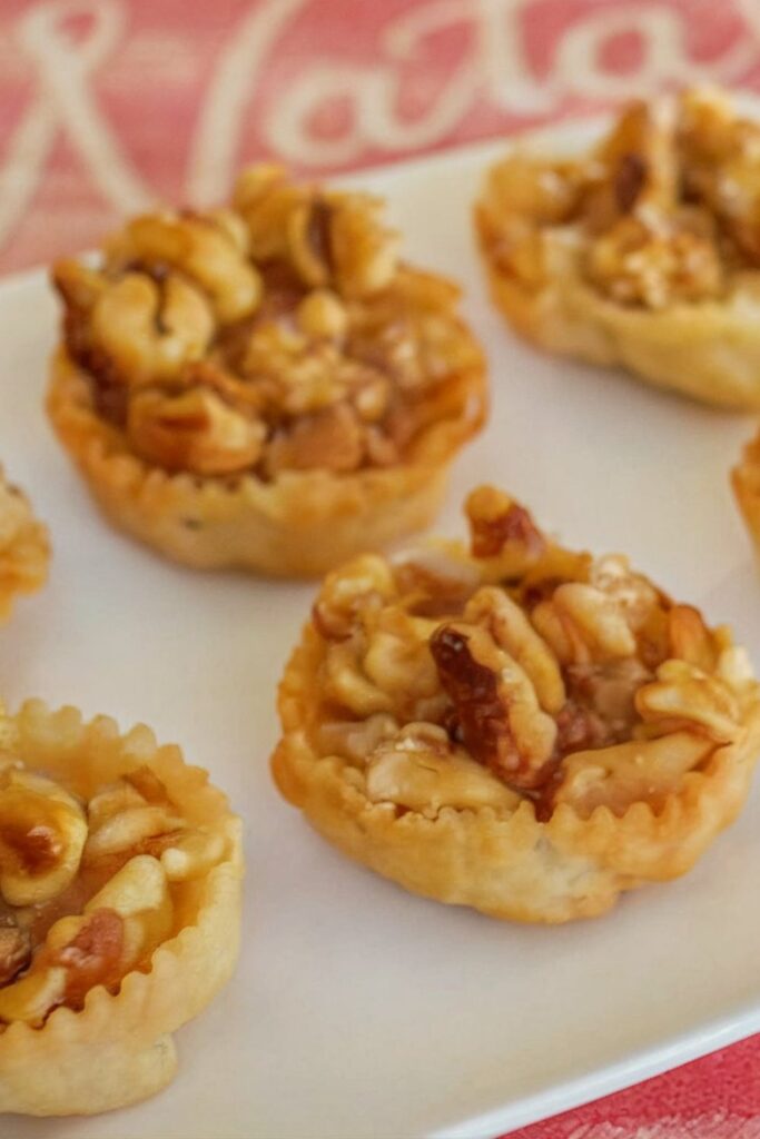 A close-up of golden, deep-fried cartellate, an authentic Italian Christmas dessert made from thin, rolled dough, drizzled with honey and topped with crunchy walnuts. These traditional Italian sweets are shaped like rosettes, perfect for festive gatherings.