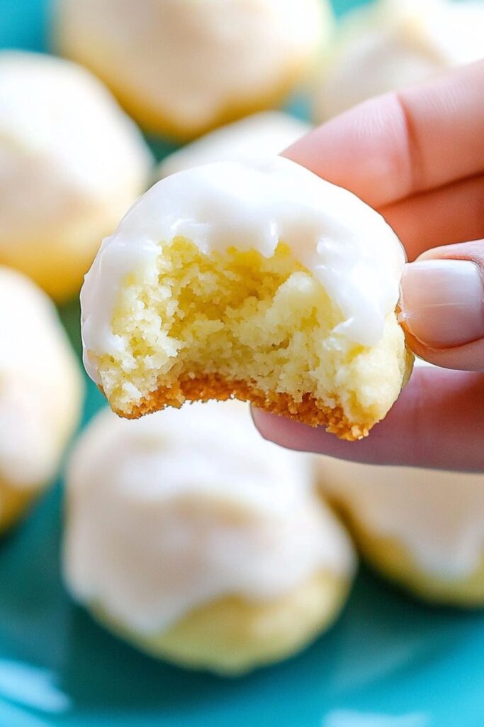 A bite-sized Italian lemon drop cookie with a tangy lemon glaze, showcasing a soft, cake-like interior, a delightful traditional Italian Christmas dessert.