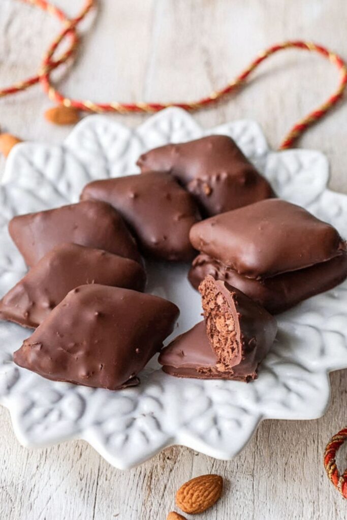 A plate of traditional Italian Mustaccioli cookies coated in dark chocolate, showcasing their soft, spiced interior and crispy outer shell, perfect for the holiday season.