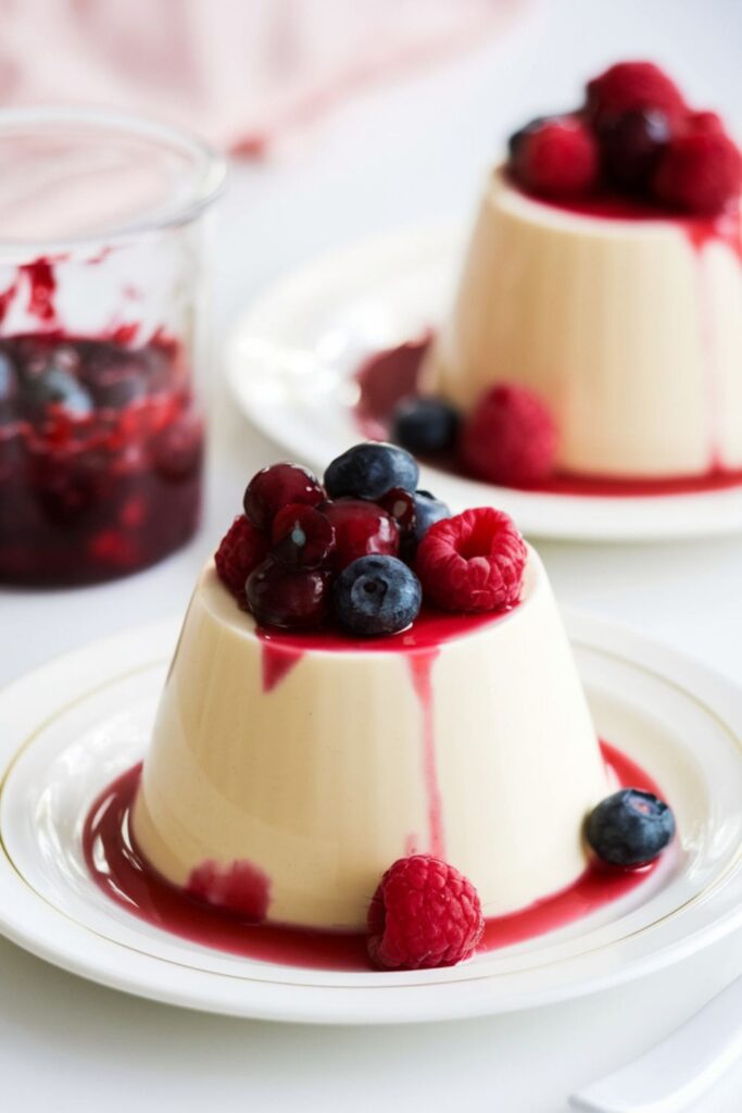 Two vanilla panna cottas topped with a mixed berry compote, served on small plates for a romantic Christmas dinner for two.