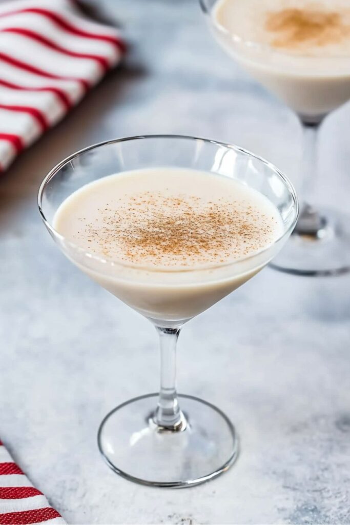 Two glasses of White Christmas Dream cocktail garnished with freshly grated nutmeg on a festive holiday table setting.