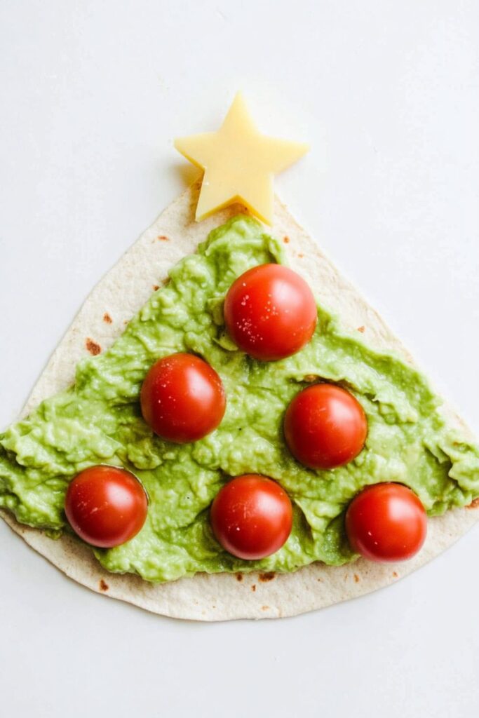 Avocado spread on a tortilla slice shaped like a Christmas tree, topped with cherry tomatoes, perfect for healthy Christmas snacks for kids.