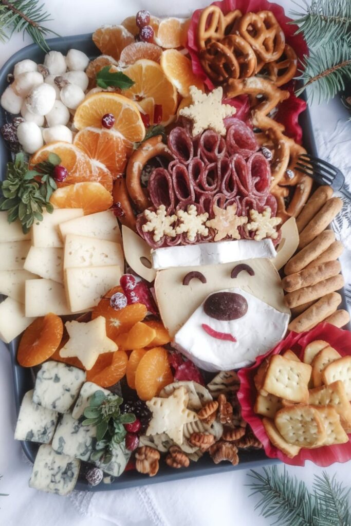 A creative Christmas reindeer charcuterie board featuring brie cheese shaped as a reindeer’s head, decorated with olives, salami, nuts, and festive garnishes like rosemary sprigs, pretzels, and cranberries.