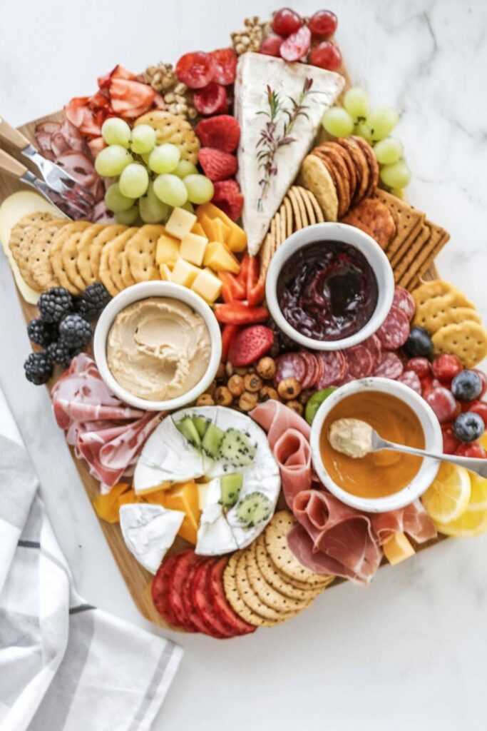 A beautifully arranged Christmas charcuterie board featuring cheese wedges, assorted nuts, fresh grapes, crackers, honey, and fig spread. Garnished with sprigs of herbs for a festive touch.