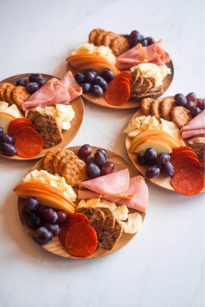 Small, festive charcuterie plates featuring sliced meats, cheeses, fruits, and crackers, perfect for individual servings at a Christmas gathering.