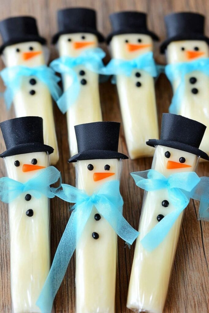 String cheese sticks decorated to look like snowmen with markers and fabric scarves, perfect for toddler Christmas snacks.