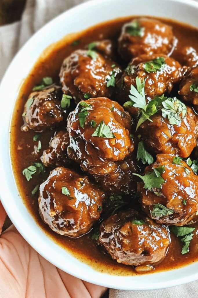 A bowl of oven-baked honey garlic meatballs coated in a glossy, sticky sauce, making them a delicious Super Bowl party food option.