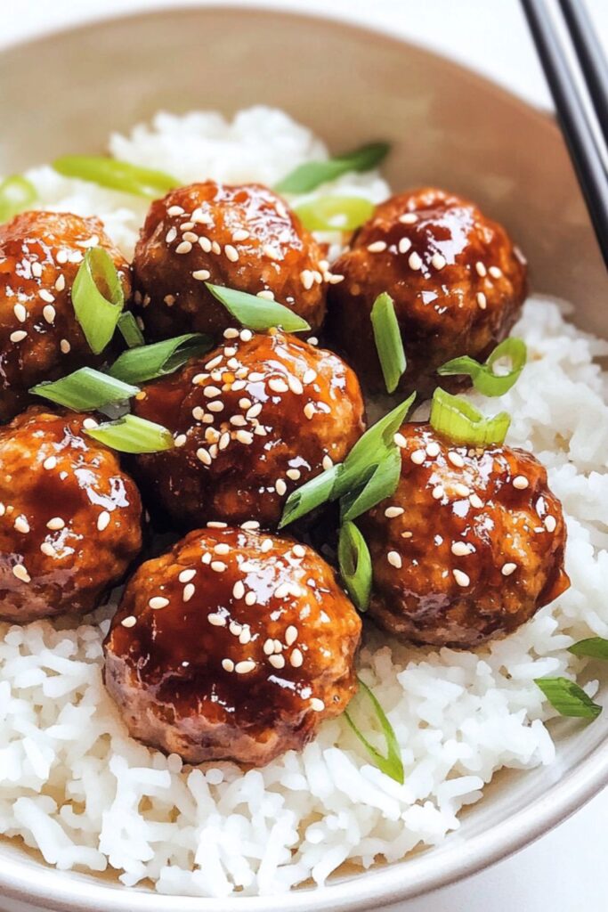 Sweet sesame ginger meatballs served on rice, garnished with sesame seeds and green onions.