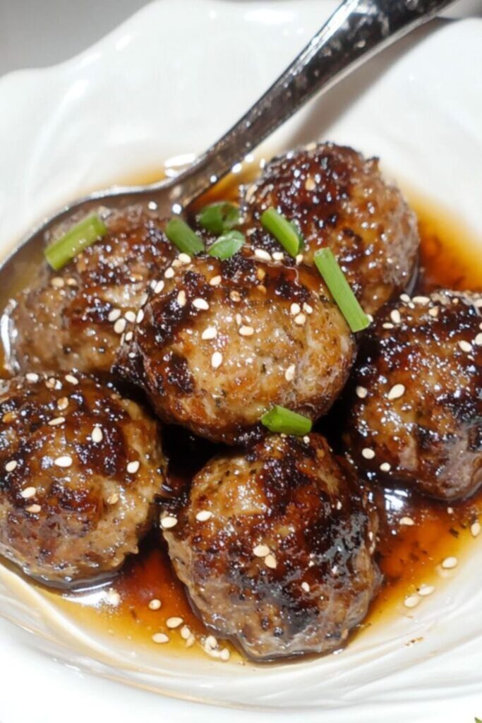 A dish of glossy teriyaki meatballs garnished with sesame seeds and green onions, offering a delicious twist for Super Bowl snacks.