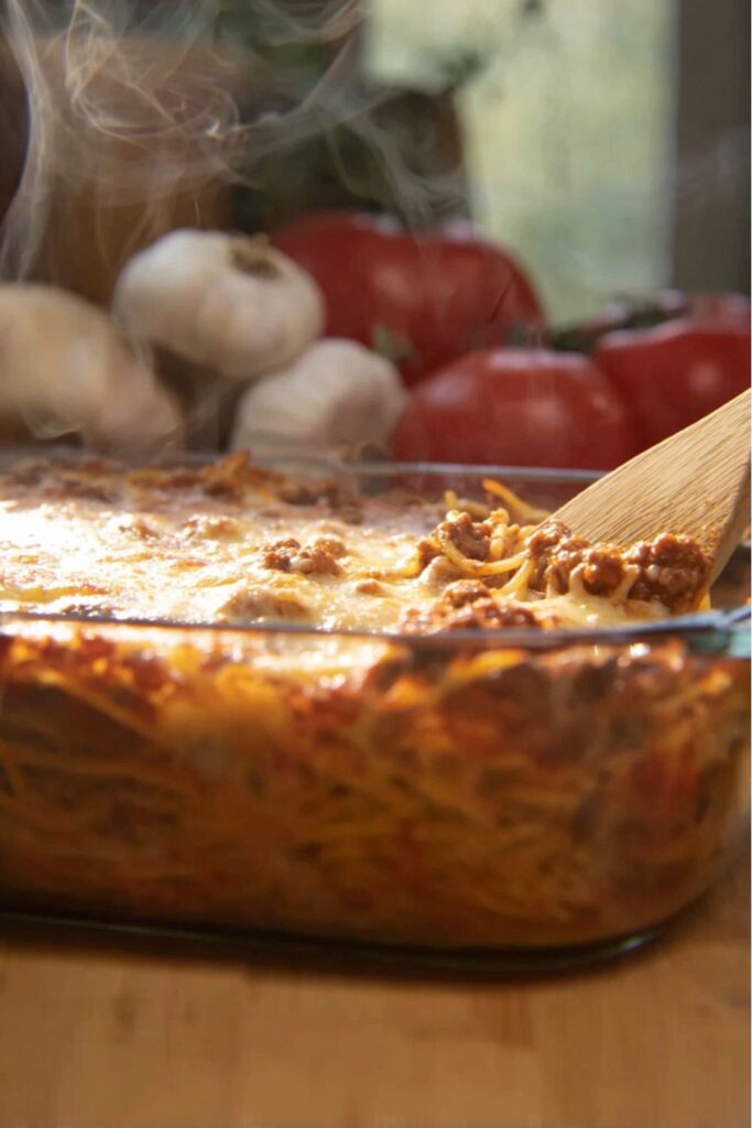 A steaming glass baking dish filled with cheesy baked spaghetti and meat sauce, perfect for hearty meat dinners.