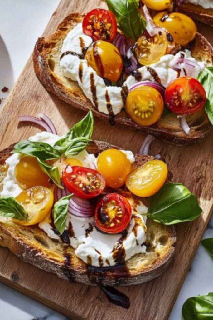 Toasted bread slices topped with creamy burrata cheese, colorful halved cherry tomatoes, red onion, and a balsamic drizzle for a spring celebration.