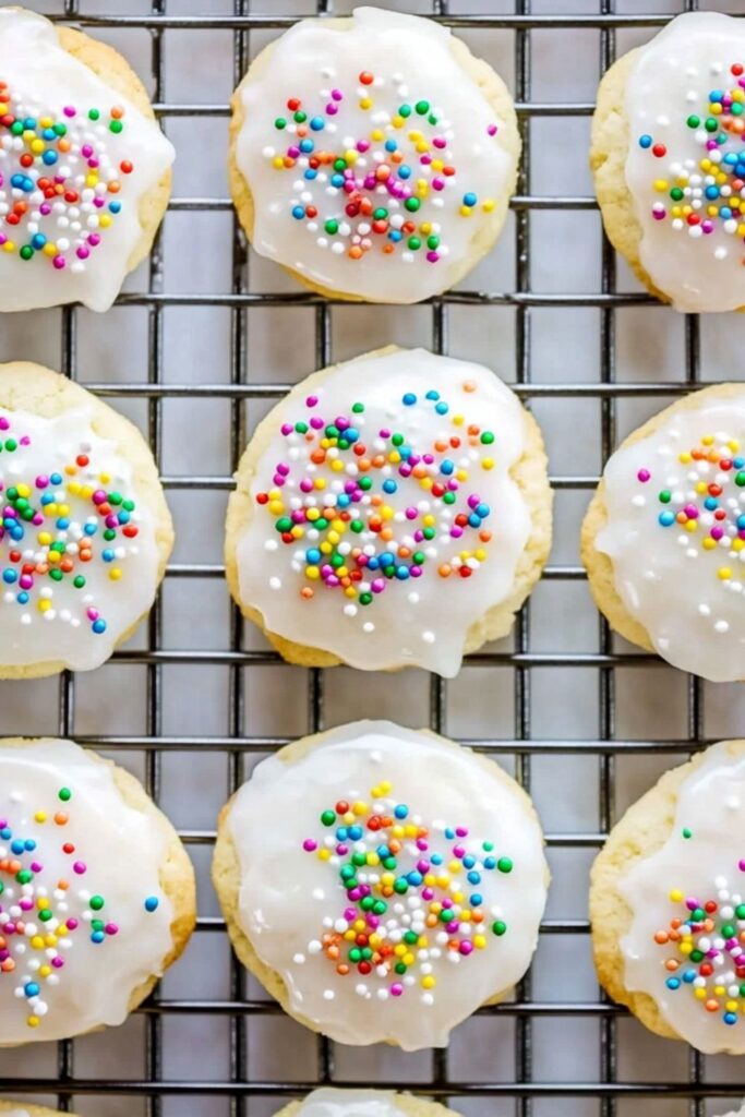 Nine round cookies topped with smooth white icing and a generous amount of rainbow sprinkles arranged on a cooling rack, perfect for a perfect easter dinner.