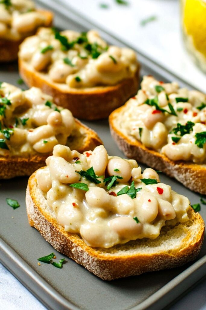 Toasted baguette slices topped with a savory smashed cannellini bean mixture and fresh parsley garnish, served as festive Easter snacks.