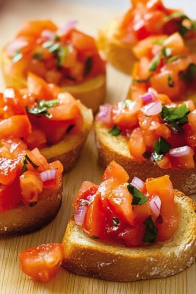 Toasted baguette slices topped with diced tomatoes, red onion, and fresh basil, served as food for easter dinner on a wooden board.